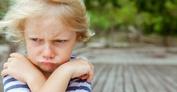 RABIETAS Face portrait of annoyed and unhappy caucasian kid with crossed arms. Upset and angry child concept for family relations, social problems issues and juvenile psychology. Copy space outdoor background.